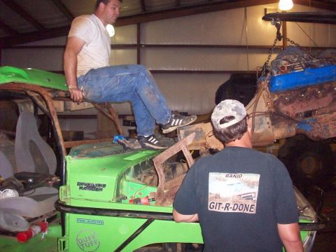 1978 Ford Bronco - Two men are working on a heavily modified green off-road vehicle inside a garage, with an engine suspended above.