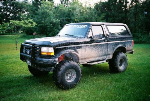 1995 Ford Bronco - Mud-covered 1995 Ford Bronco with lifted suspension and off-road tires sits on a grassy lawn.