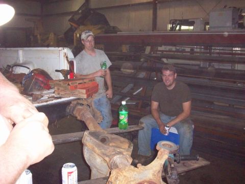 1978 Ford Bronco - Two men take a break with pizza in a workshop, with a truck bed and various metal parts visible.