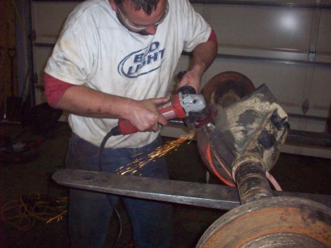 1978 Ford Bronco - Man working on a vehicle axle with an angle grinder, sparks flying.