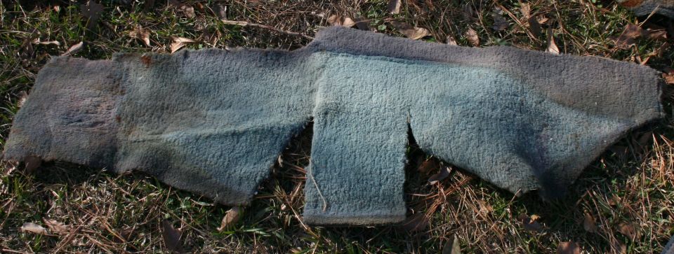 Worn, cut piece of blue and gray carpet lying on grass and leaves
