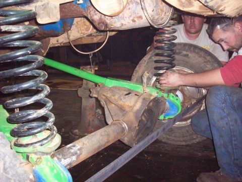 1978 Ford Bronco - Two individuals are shown working on the undercarriage of a vehicle, focusing on the suspension system and axle components.