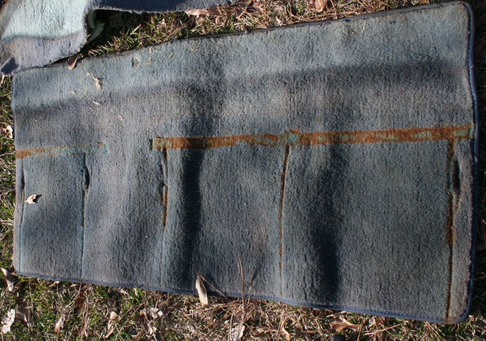 Faded blue-gray vehicle carpet piece with rust stains laid on grass