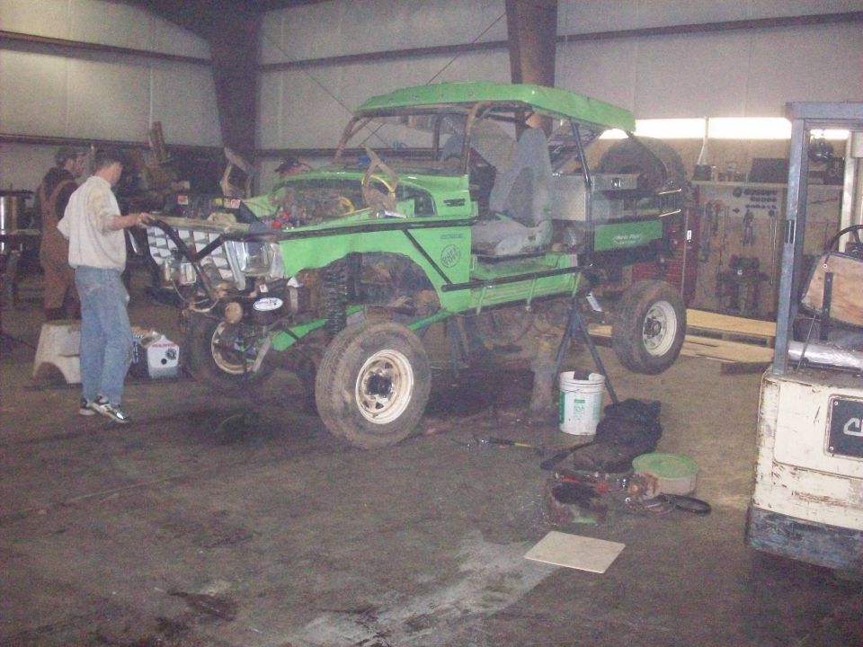 Green 1978 Ford Bronco with custom roll cage and off-road modifications, lifted and on stands in a workshop