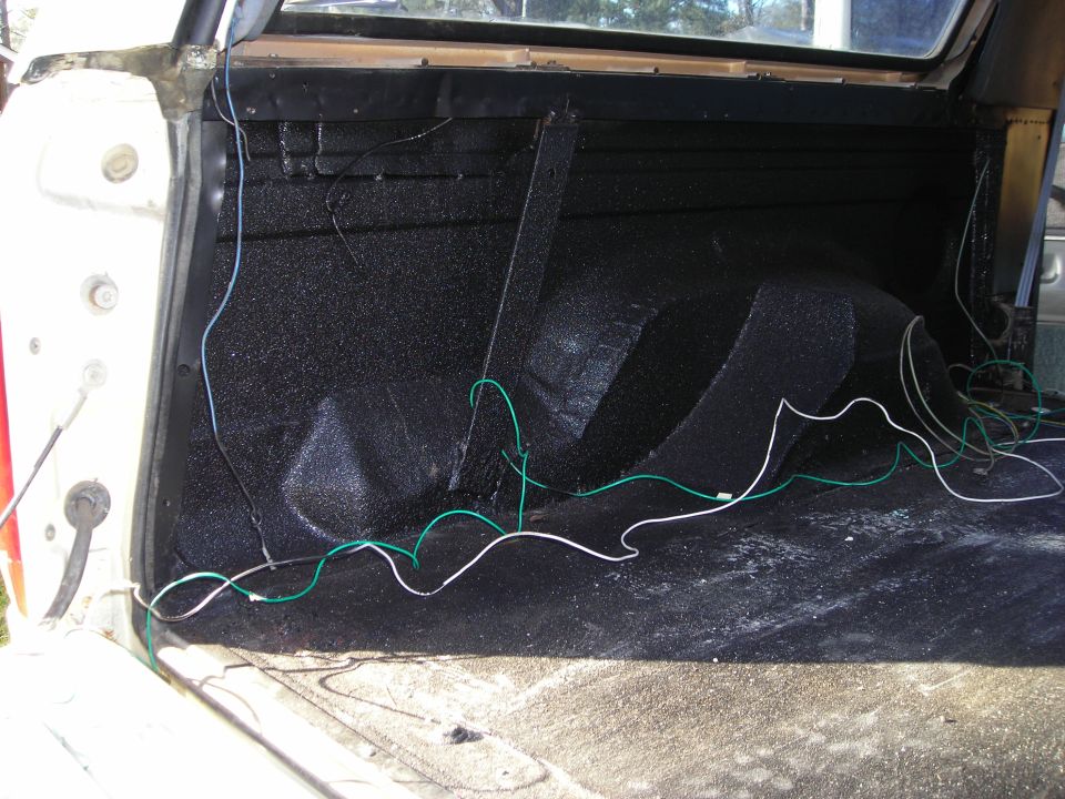 Interior of a pickup truck bed with black textured liner and wires.