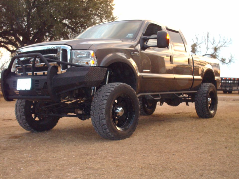 Brown Ford F-250 pickup truck with aftermarket bumper and large tires.
