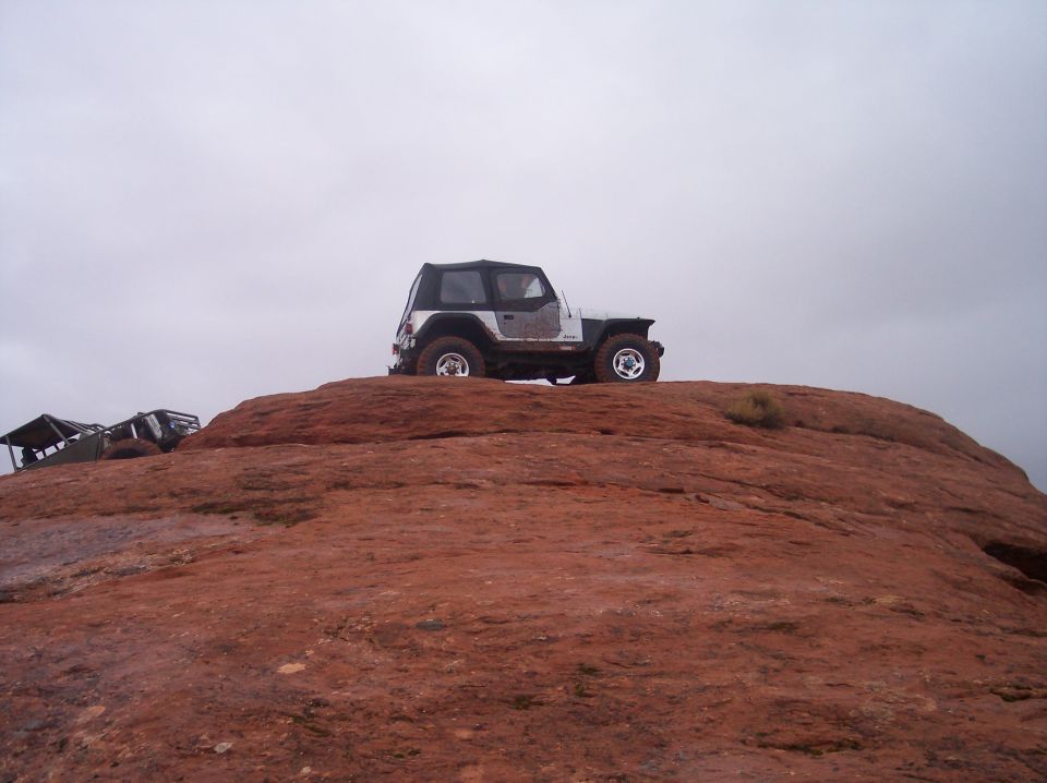 White Jeep Wrangler on a red rock formation with another off-road vehicle in the background.