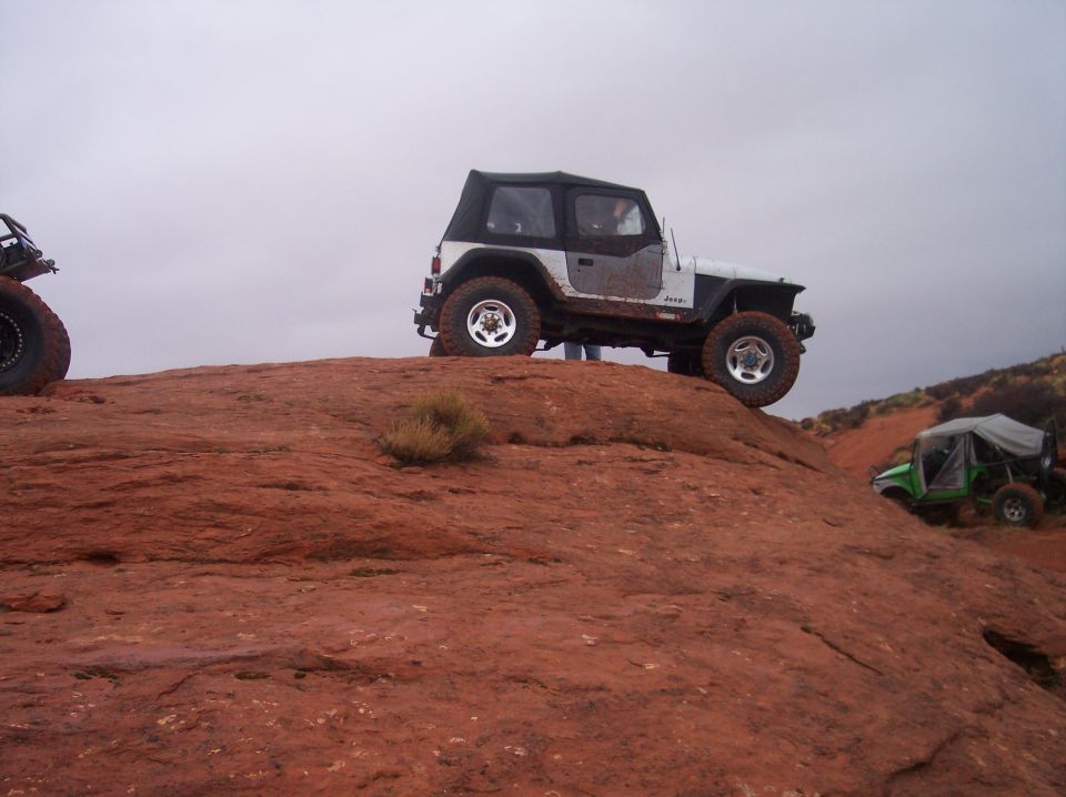 White Jeep Wrangler and green off-road vehicle on red rocks.