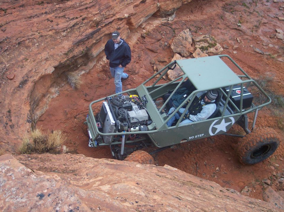 Olive drab buggy with roll cage and exposed engine on a rocky red dirt trail.