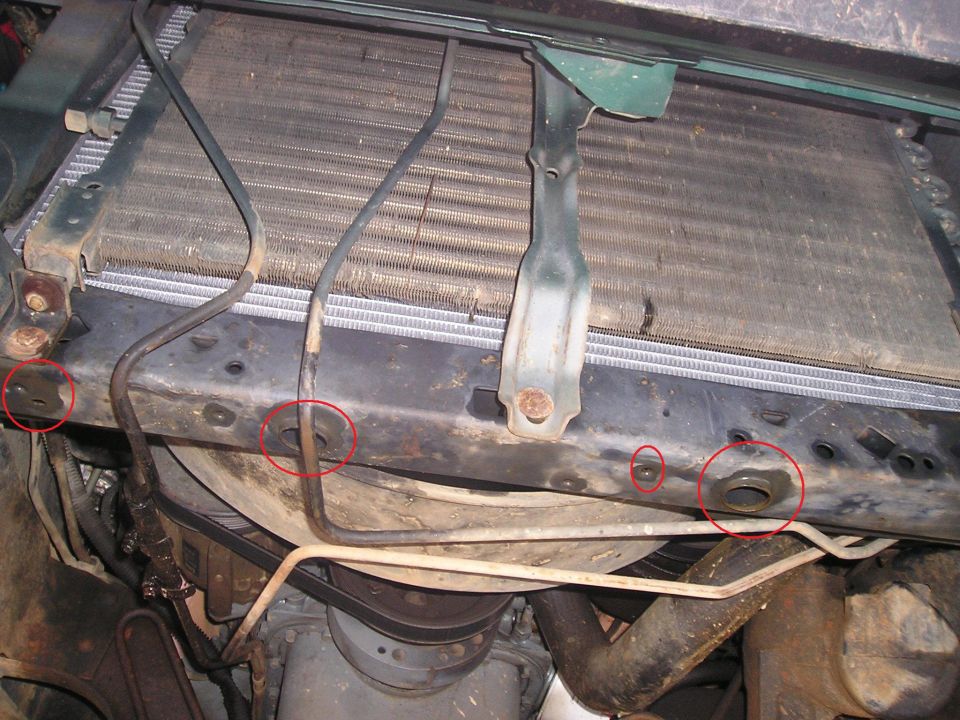 Close-up of vehicle radiator support showing rust and wear.