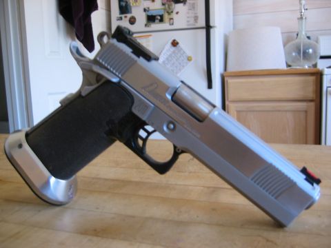 1996 Ford Bronco - A close-up, side profile of a silver and black handgun resting on a wooden table. The handgun has a textured black grip and a silver frame…