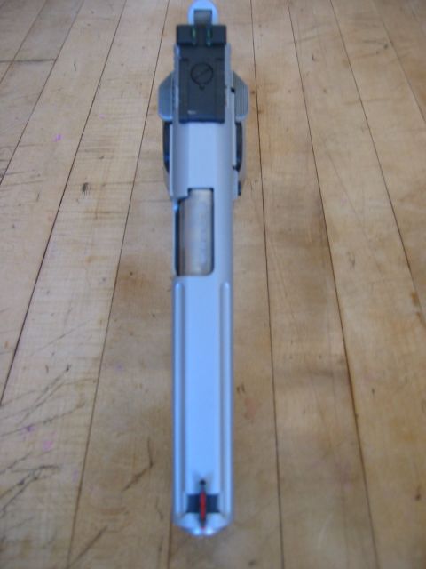 1996 Ford Bronco - This is a top-down view of a silver pistol lying on a wooden surface. The pistol has black sights on the rear and a red and black front sig…