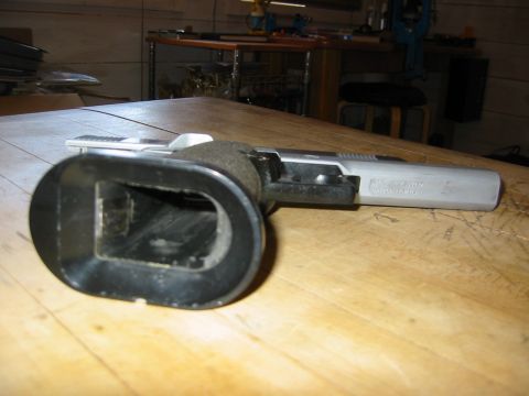 1996 Ford Bronco - A close-up view of a firearm with a black magazine extension and a silver slide rests on a wooden table. The firearm is positioned at an an…