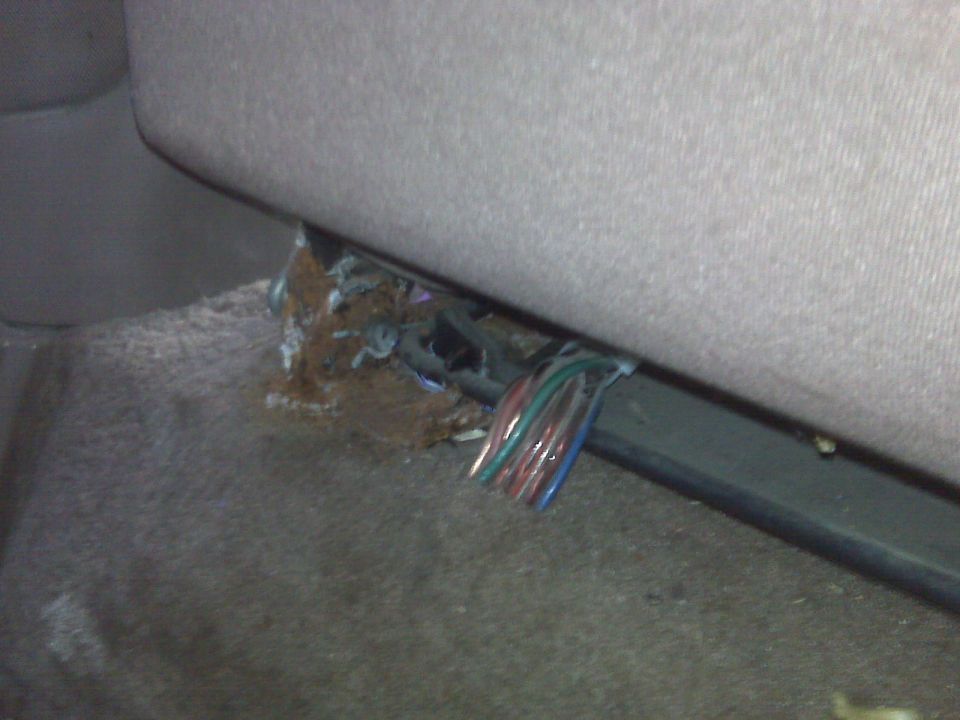 Wires with red, green, and blue insulation under a vehicle seat.