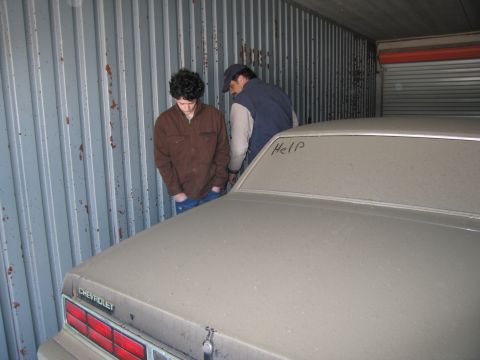 1991 Ford LTD Crown Victoria - Photograph of two people next to a dust-covered Chevrolet in a storage container, not a technical document.