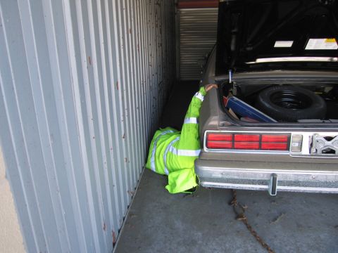 1991 Ford LTD Crown Victoria - Photograph of a person in a hi-vis jacket beside a stored sedan with open trunk, not a technical document.
