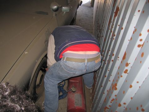 1991 Ford LTD Crown Victoria - Photo of a person bent over a propane tank working on a car's front wheel inside a storage container.