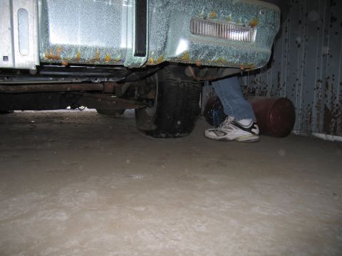 1991 Ford LTD Crown Victoria - Photo of a car's lower front bumper and wheel from ground level inside a dim storage container.