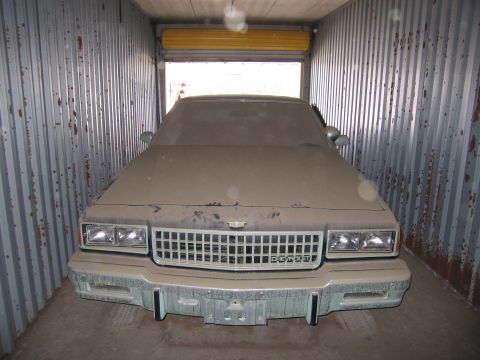 1991 Ford LTD Crown Victoria - Photo of a heavily dust-covered tan Chevrolet sedan facing the open door of a storage container.