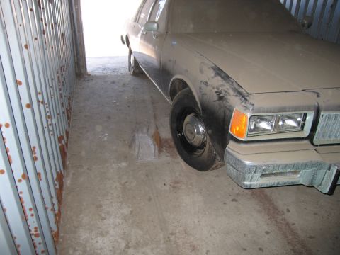 1991 Ford LTD Crown Victoria - Photo of the front fender and wheel of a tan Chevrolet sedan in a narrow storage container.