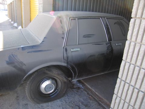 1991 Ford LTD Crown Victoria - Photo of the rear side of a black Chevrolet sedan parked beside a self-storage unit.