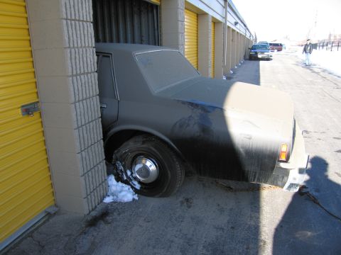 1991 Ford LTD Crown Victoria - Photo of a black sedan with a shredded front tire being pulled from a yellow-door storage unit.