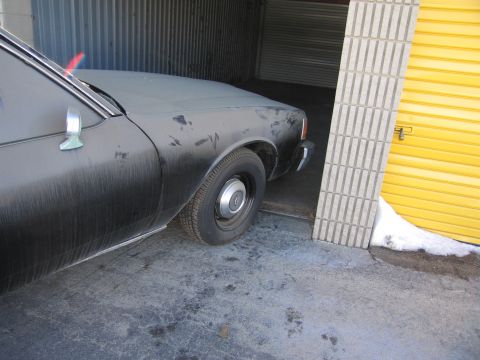 1991 Ford LTD Crown Victoria - Photo of the front fender and wheel of a black sedan parked next to a yellow storage door.