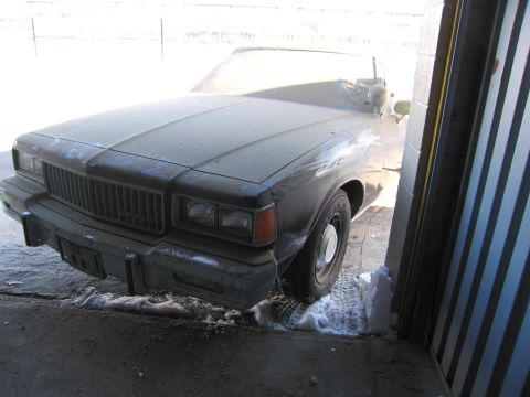1991 Ford LTD Crown Victoria - Photo of the snow-dusted front of a black Chevrolet sedan partly inside a garage doorway.