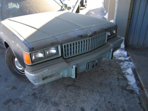 1991 Ford LTD Crown Victoria - Photo of the dust-covered front grille and bumper of a Chevrolet sedan by a garage doorway.