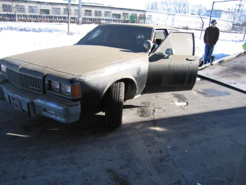 1991 Ford LTD Crown Victoria - Photo of a dusty Chevrolet sedan with its door open being loaded on a flatbed in a snowy lot.