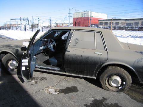 1991 Ford LTD Crown Victoria - Photo of a dusty black Chevrolet sedan with its driver door open in a snowy industrial lot.