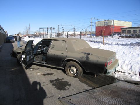 1991 Ford LTD Crown Victoria - Photo of a dust-covered Chevrolet sedan with door open on a flatbed tow truck in a snowy lot.