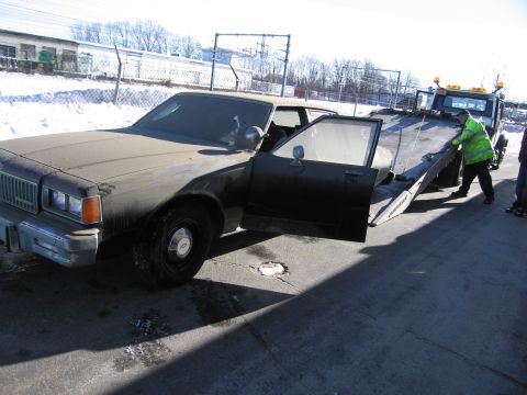 1991 Ford LTD Crown Victoria - Photograph of a grimy Chevrolet Caprice sedan being winched onto a flatbed tow truck on a snowy lot.