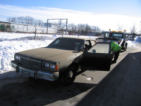 1991 Ford LTD Crown Victoria - Photograph of a dirty Chevrolet Caprice sedan parked beside a flatbed tow truck in a snowy yard.