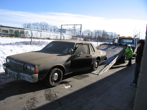 1991 Ford LTD Crown Victoria - Photograph of a dusty Chevrolet Caprice sedan being loaded up the tilted bed of a flatbed tow truck.