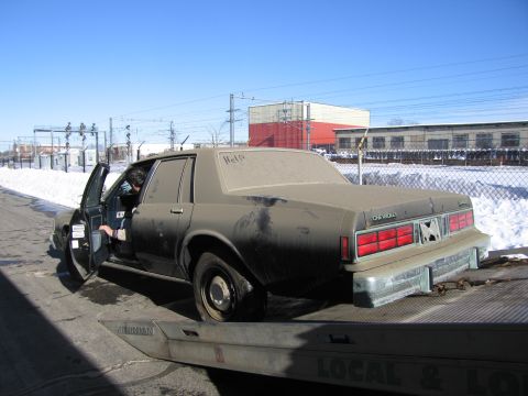1991 Ford LTD Crown Victoria - Photograph of the rear of a grimy Chevrolet Caprice on a flatbed tow truck with words drawn in road dust.