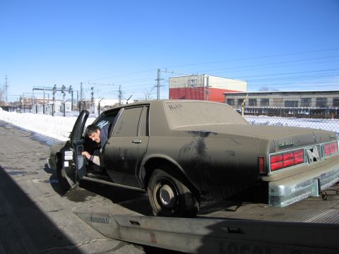 1991 Ford LTD Crown Victoria - Photograph of a man at the driver door of a grimy Chevrolet Caprice secured on a flatbed tow truck.