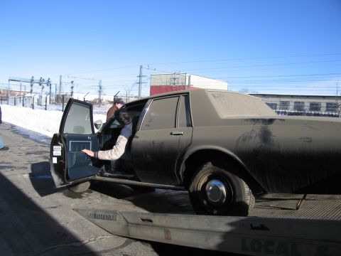 1991 Ford LTD Crown Victoria - Photograph of a person climbing out of a grimy Chevrolet Caprice loaded on a flatbed tow truck.
