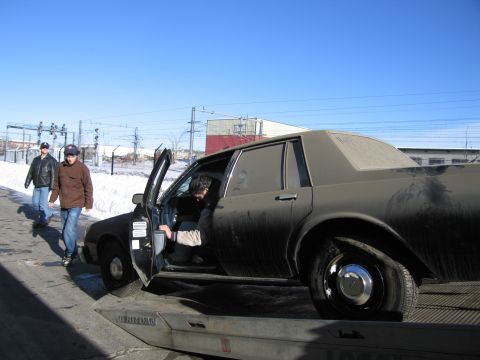 1991 Ford LTD Crown Victoria - Photograph of bystanders near a dirty Chevrolet Caprice while a person enters it on the tow truck bed.