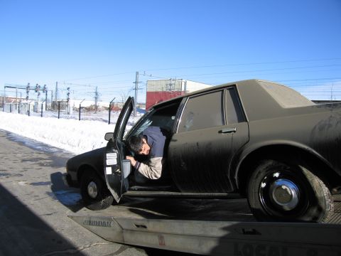 1991 Ford LTD Crown Victoria - Photograph of a man reaching into the driver door of a grimy Chevrolet Caprice on a flatbed tow truck.