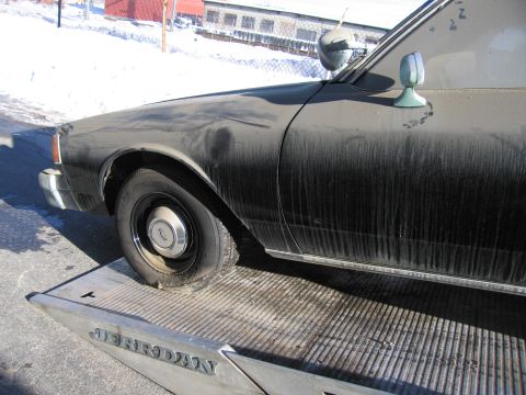 1991 Ford LTD Crown Victoria - Photograph of the dirty front wheel, fender and Chevrolet badge of a Caprice resting on a flatbed tow truck.
