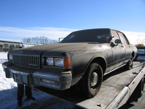 1991 Ford LTD Crown Victoria - Photograph of a grimy Chevrolet Caprice sedan secured on a flatbed tow truck in a snowy lot.