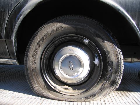 1991 Ford LTD Crown Victoria - Photograph of a grimy Goodyear Eagle GT tire and Chevrolet wheel cover resting on a flatbed tow truck.