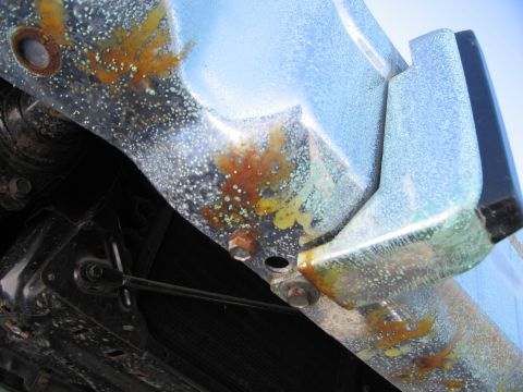 1991 Ford LTD Crown Victoria - Photograph of a corroded underbody panel and a metal line on the underside of a vehicle.