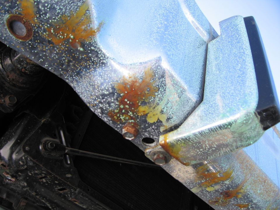 Underside close-up of a rusty metal floor pan and brake or fuel line