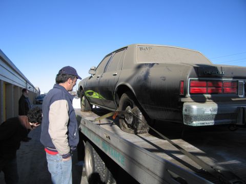 1991 Ford LTD Crown Victoria - Photograph of a man inspecting the rear of a grimy Chevrolet Caprice strapped on a flatbed tow truck.