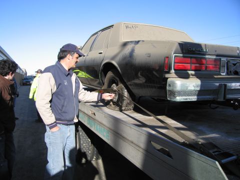 1991 Ford LTD Crown Victoria - Photograph of a man securing a tie-down strap on a dirty Chevrolet Caprice on a flatbed tow truck.