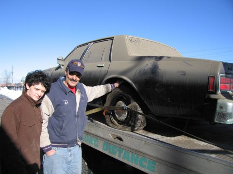1991 Ford LTD Crown Victoria - Photograph of two people standing beside a grimy Chevrolet Caprice loaded on a flatbed tow truck.