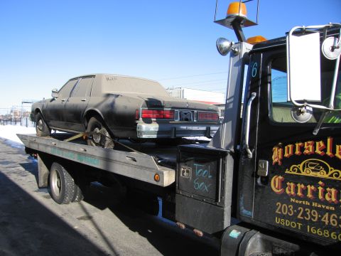 1991 Ford LTD Crown Victoria - Photograph of a black full-size sedan strapped to a flatbed tow truck, not a technical document.
