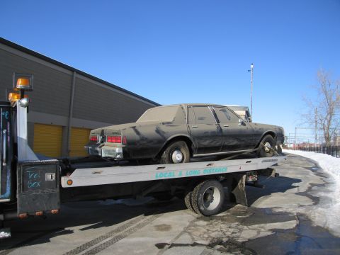 1991 Ford LTD Crown Victoria - Photograph of a black sedan on a flatbed tow truck beside a storage building, not a technical document.